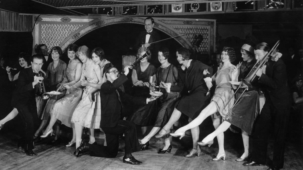 Female flappers kicking, dancing, and having fun while musicians perform during a Charleston dance contest at the Parody Club